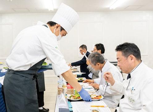審査員の前に料理を置く学生たち